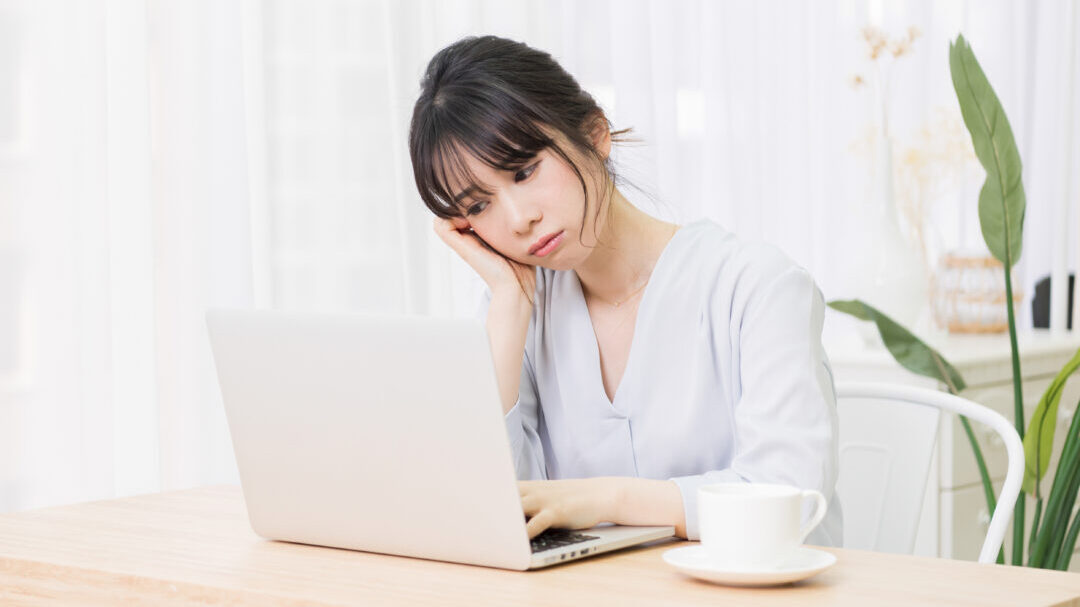 部屋でノートパソコンを使いながら悩む女性